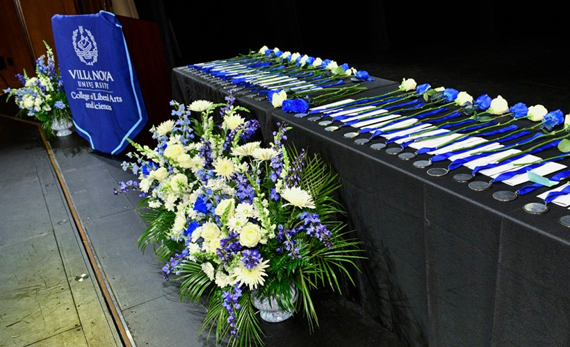 A table with medallion awards on a stage with blue and white flowers. A table with medallion awards on a stage with blue and white flowers.